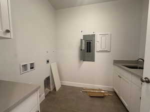 Washroom featuring hookup for an electric dryer, electric panel, hookup for a washing machine, dark tile patterned floors, and cabinet space