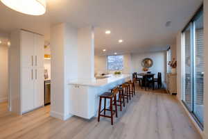 Kitchen featuring white cabinetry, stainless steel dishwasher, a kitchen breakfast bar, and light hardwood / wood-style flooring