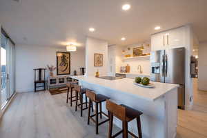 Kitchen featuring white cabinets, a breakfast bar, stainless steel fridge, and light wood-type flooring