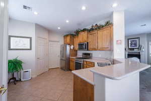 Kitchen featuring sink, light tile patterned floors, stainless steel appliances, light stone counters, and kitchen peninsula