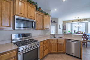 Kitchen featuring sink, stainless steel appliances, a notable chandelier, a healthy amount of sunlight, and kitchen peninsula