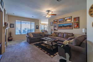 Living room with ceiling fan, carpet flooring, and a textured ceiling