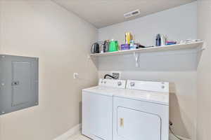 Laundry area with washing machine and dryer, light tile patterned floors, and electric panel