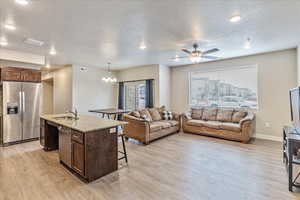 Kitchen featuring pendant lighting, sink, stainless steel fridge, light stone counters, and a center island with sink