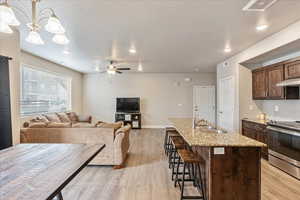 Kitchen featuring sink, hanging light fixtures, light stone counters, a center island with sink, and stainless steel range with electric cooktop