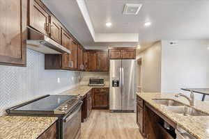 Kitchen with light stone counters, sink, light hardwood / wood-style flooring, and stainless steel appliances