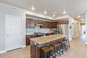 Kitchen featuring sink, appliances with stainless steel finishes, light hardwood / wood-style floors, an island with sink, and a kitchen bar