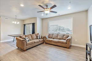 Living room with ceiling fan with notable chandelier and light wood-type flooring