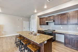 Kitchen featuring sink, light stone countertops, a breakfast bar, and a center island with sink