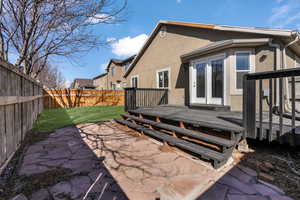 Back of property with a wooden deck, a patio, a fenced backyard, a yard, and stucco siding