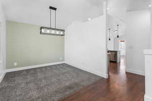 Empty room featuring lofted ceiling, wood walls, dark wood-style flooring, and baseboards