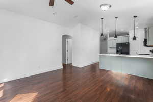 Kitchen with arched walkways, a ceiling fan, dark wood-type flooring, light countertops, and black appliances