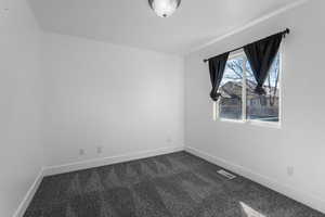 Spare room with visible vents, dark carpet, and baseboards