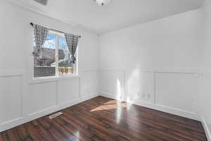 Empty room featuring a wainscoted wall, visible vents, and wood finished floors