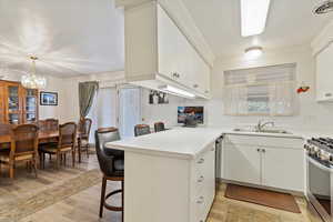 Kitchen featuring white cabinetry, sink, ornamental molding, kitchen peninsula, and gas range