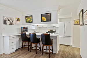 Kitchen featuring a breakfast bar area, white refrigerator, stainless steel range, kitchen peninsula, and white cabinets