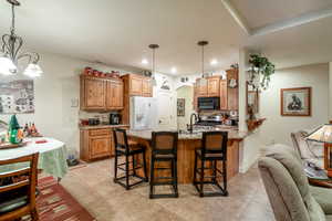 Kitchen with light stone countertops, white fridge with ice dispenser, pendant lighting, and a kitchen bar