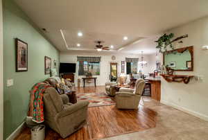 Living room with a tray ceiling, ceiling fan with notable chandelier, and light hardwood / wood-style floors