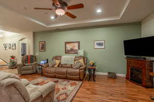 Living room with light hardwood / wood-style flooring, a raised ceiling, and ceiling fan