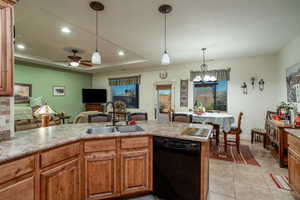 Kitchen featuring light tile patterned floors, sink, black dishwasher, decorative light fixtures, and a raised ceiling