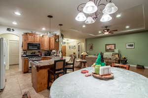 Dining space with sink, ceiling fan with notable chandelier, a raised ceiling, and light tile patterned floors