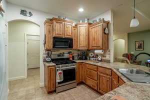 Kitchen featuring sink, light tile patterned floors, backsplash, hanging light fixtures, and stainless steel gas range oven