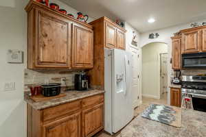 Kitchen with stainless steel gas range oven, white fridge with ice dispenser, light tile patterned floors, and decorative backsplash