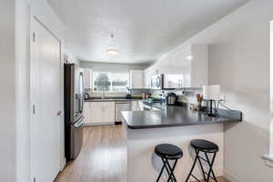 Kitchen with appliances with stainless steel finishes, a breakfast bar, white cabinetry, sink, and kitchen peninsula