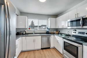 Kitchen with sink, a textured ceiling, appliances with stainless steel finishes, light hardwood / wood-style floors, and white cabinets