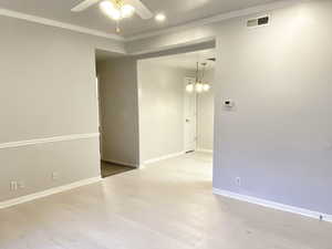 Spare room featuring crown molding, ceiling fan with notable chandelier, and hardwood / wood-style flooring