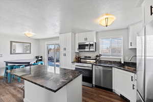 Kitchen with dark wood-type flooring, sink, white cabinetry, dark stone countertops, and stainless steel appliances