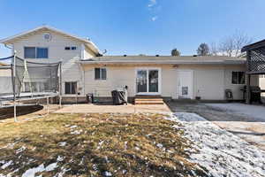 Snow covered back of property featuring a yard, a patio area, and a trampoline