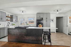 Kitchen with sink, light hardwood / wood-style flooring, gray cabinetry, black fridge, and stainless steel dishwasher