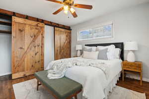 Bedroom featuring ceiling fan, a barn door, and dark hardwood / wood-style flooring