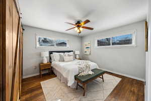 Bedroom with dark wood-type flooring, a barn door, and ceiling fan