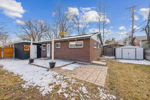 Snow covered rear of property with a patio area and a storage shed