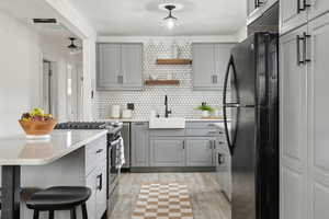 Kitchen with gray cabinetry, sink, stainless steel gas range oven, and black fridge