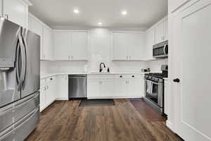 Kitchen with stainless steel appliances, sink, dark wood-type flooring, and white cabinets