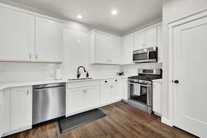 Kitchen with sink, dark wood-type flooring, appliances with stainless steel finishes, white cabinetry, and backsplash