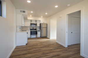 Kitchen with sink, appliances with stainless steel finishes, white cabinetry, dark hardwood / wood-style floors, and decorative backsplash