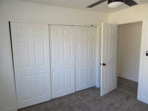 Unfurnished bedroom with ceiling fan, dark carpet, and a closet