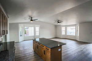 Kitchen with ceiling fan, dark hardwood / wood-style floors, a center island, and dark stone counters