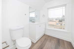 Bathroom with hardwood / wood-style flooring, vanity, lofted ceiling, and toilet