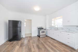 Kitchen with dark wood-type flooring, sink, black refrigerator, electric stove, and white cabinets