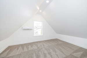 Additional living space featuring lofted ceiling, a wall mounted air conditioner, and carpet flooring