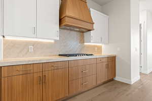 Kitchen featuring stainless steel gas stovetop, white cabinets, backsplash, custom range hood, and light wood-type flooring