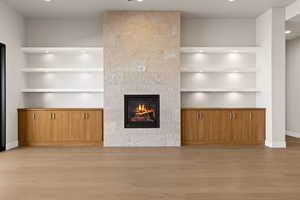 Unfurnished living room featuring built in shelves, a fireplace, and light hardwood / wood-style flooring