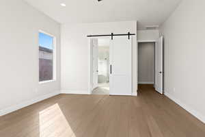 Unfurnished bedroom with ensuite bath, a barn door, and light hardwood / wood-style flooring