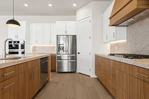 Kitchen with sink, custom exhaust hood, hanging light fixtures, stainless steel appliances, and white cabinets