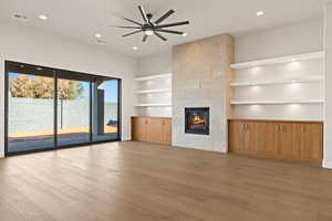 Unfurnished living room featuring ceiling fan, built in features, a fireplace, and light hardwood / wood-style flooring